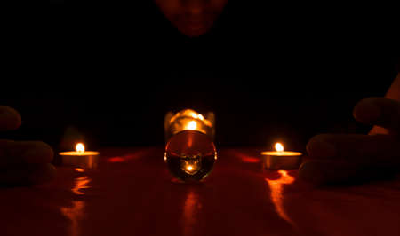 A mysterious man in black is performing a ritual, using candles and crystal balls for superstitions.