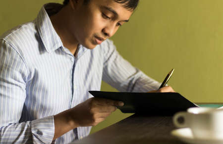 Asian men are working and writing notes on notebooks and coffee on a relaxed work day.の写真素材