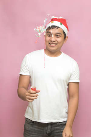 Asian man wearing santa claus hat celebrating christmas with explosive confetti on pink backgroundの写真素材