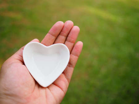 Female hand holding a white ceramic heart on garden backgroundの写真素材