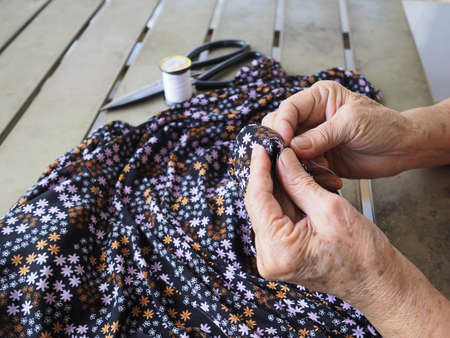 Asian elderly woman hands sewing cloth outdoors