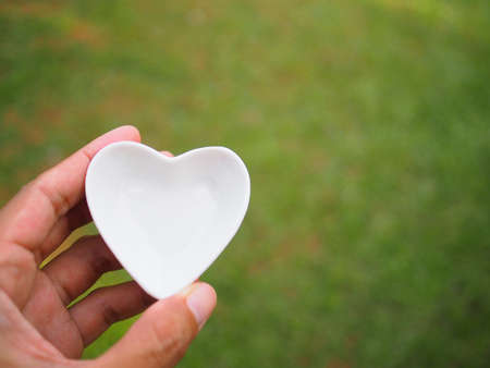 Female hand holding a white ceramic heart on garden backgroundの写真素材