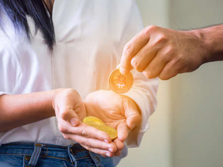 Hand of man putting golden bitcoin on women's palm against white background.の写真素材