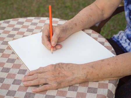 Hands of elderly woman writing a book at the table in the garden.の写真素材