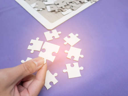 Closeup hand of man connecting jigsaw puzzle with sunlight effect.