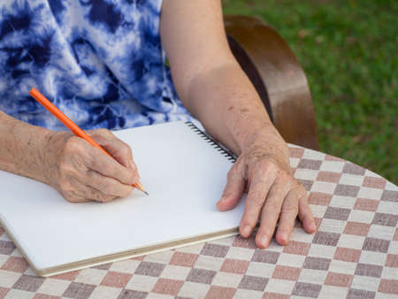 Hands of elderly woman writing a book at the table in the garden.の写真素材