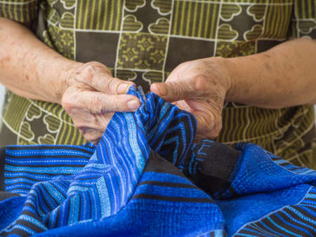 Close up of older woman's hands using razor to mend a clothの写真素材