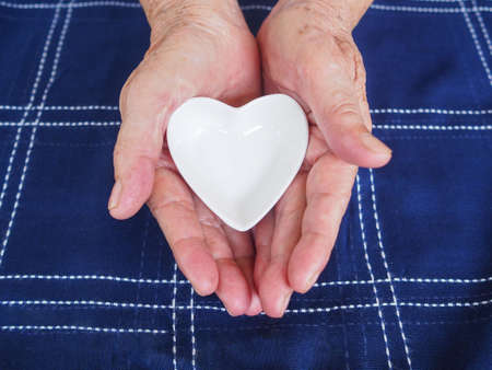 Close-up partial view of white ceramic heart in senior woman hands. Love Concept.