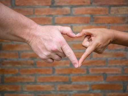 Close-up of making heart shape with hands between man and woman with brick background. Love Concept.の写真素材