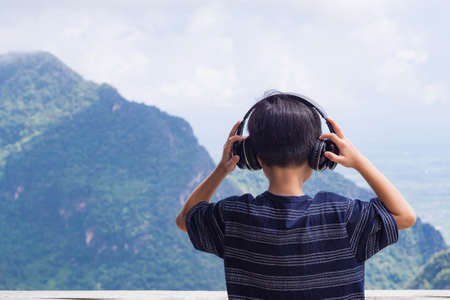 Back view of boy kid standing listen favorite song with wireless headphone and enjoy by looking to...