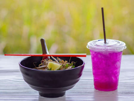 Close-up of Noodle Soup in black cup with red chopsticks and Herb water on white wooden table.