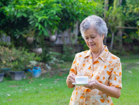Portrait of happy senior woman holding white cup in the garden.の写真素材