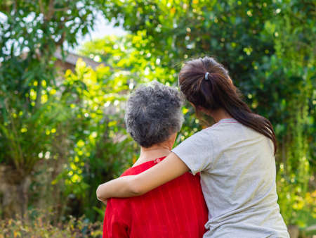 Back view of young woman hugging her grandmother in garden.の写真素材