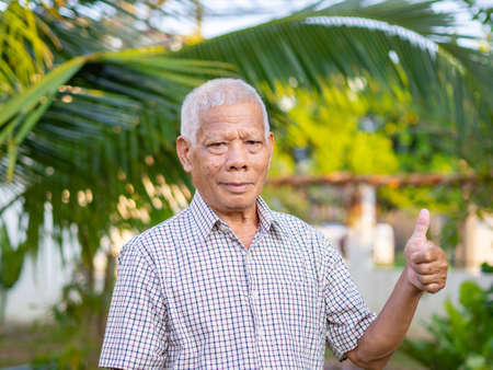 Cheerful senior man showing thumb up gesture in his garden.の写真素材