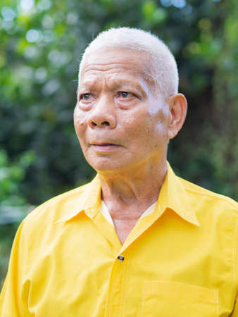 Portrait of an senior man wearing a yellow shirt and looking up while standing in a garden.の写真素材