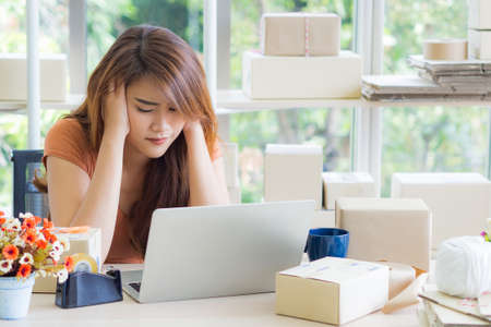 Young business woman having headache while working on laptop in the office. Feeling tired and stressed about her working problems. Business conceptの写真素材