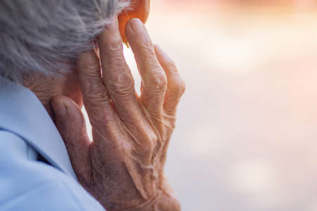 Back view of elderly woman hand touch in the ear her. Focus on hands wrinkled skin. Health care...