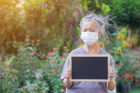 Portrait of an elderly woman standing holding a blackboard and wearing face mask for healthy because have air pollution PM 2.5. Mask for protect Virus, Bacteria, Pollen Grains. Healthcare conceptの写真素材