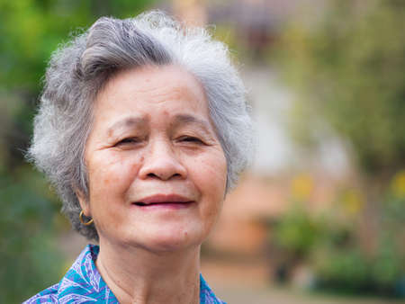 Portrait of elderly woman with short white hair and standing smile in garden. Asian senior woman...