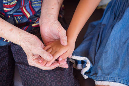 Close-up shot of grandma holding hands in granddaughter. Concept of old people and children.