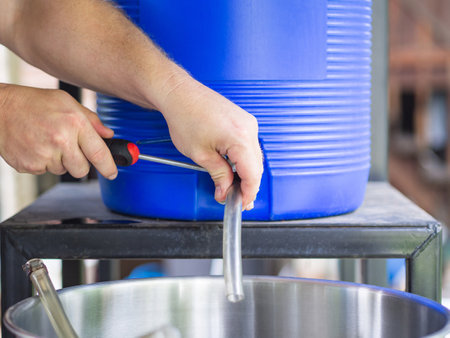 Close-up of young man hands holding a screwdriver to tighten the rubber strap to let the craft beer flow out. Selective focus. Home brewing process.の写真素材
