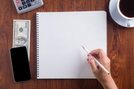 Close-up of a woman right hand holding a pencil preparation for drawing on sketchbook on wood desk. Wood texture background. Concept of drawing and technologyの写真素材