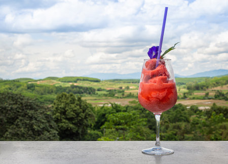 Fresh healthy watermelon smoothie in glass against the background of sky, clouds and mountains. Healthy nutrition and vitaminsの写真素材