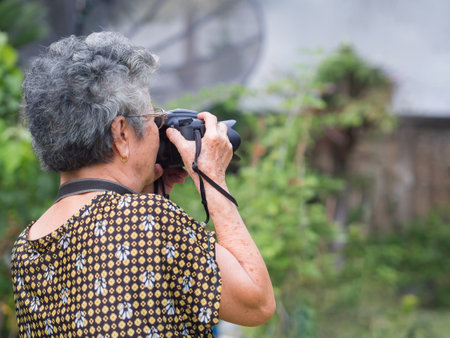 Elderly woman shooting photo by digital camera at garden. Asian senior woman short white hair, wearing eyeglasses, happy when using a camera. Concept of old people and photographyの写真素材