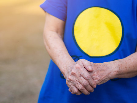 Close-up of an elderly woman hands joined together with sunlight. Focus on hands wrinkled skin. Space for text. Health care conceptの写真素材
