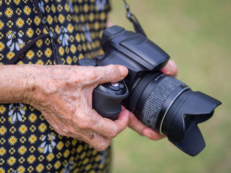Close-up of hands a senior woman holding the digital camera while standing in a garden. Concept of aged people and photography.の写真素材