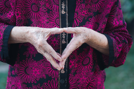 Close-up of hand senior woman's making a heart symbol while standing in the garden. Space for text. Concept of aged people and healthcare.の写真素材