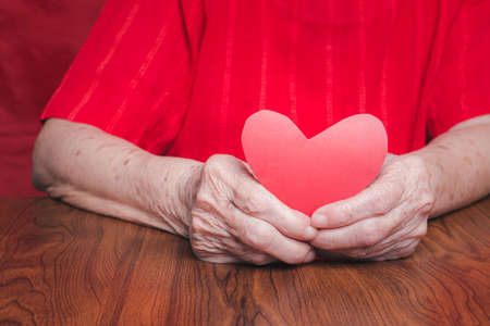 Red paper cut heart shape hold by hand senior woman. Valentine's day. Concept of aged people and love.の写真素材