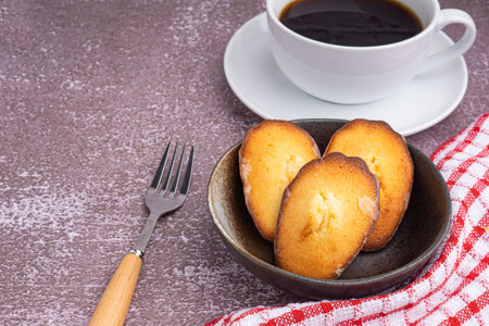 Madeleine homemade traditional French small cookies on black a dish and a coffee cup placed on a...