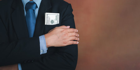 Businessman wearing a suit with US dollars in a suit pocket and arms crossed while standing in a...