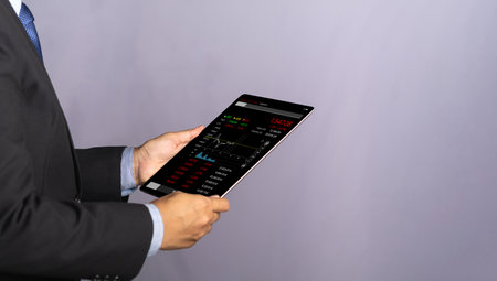 Side view of a businessman holding and reading business graphs and stock charts on a digital tablet. Stock market investments funds and digital assets. Business finance and investment concept.の写真素材