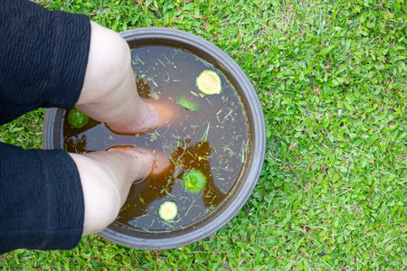 Close-up of the foot spa with herbs water for relaxation treatment. A senior woman who has ankle pain uses herbal treatment to relax the muscles by soaking warm water that is boiled from herbs.の写真素材