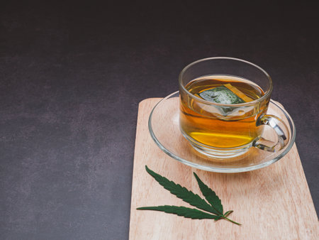 A cup of hemp tea and marijuana leaf laid on a wooden cutting board with a vintage background. Cannabis herbal tea. Close-up photo. Selective focus. Relaxation concept.の写真素材