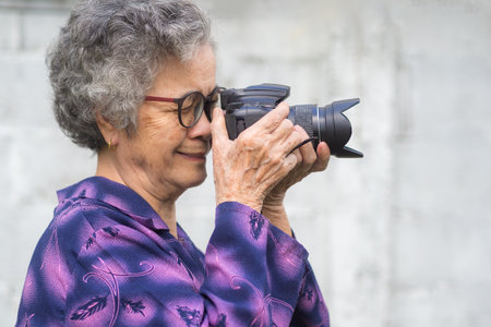 Happy senior woman taking photographs with a digital camera while standing outdoors. Aged people photographer and relaxation concept.の写真素材