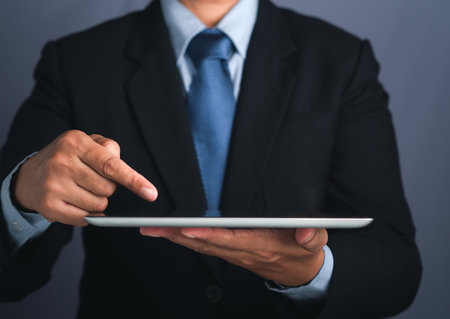 Hand of a businessman holding a digital tablet and touching on the screen. Close-up photo. Business and technology concept.の写真素材