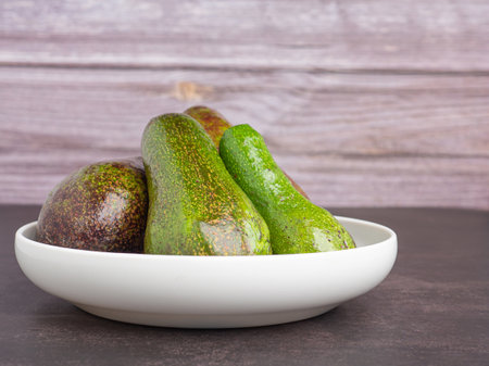 Avocados are served on a white plate with a wooden background. Side view. Space for text. Healthy...