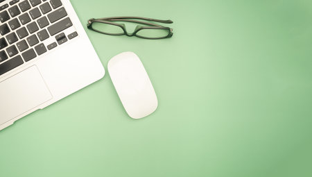 Top view of a laptop, mouse, and glasses isolated on a green background with space for text. Technology and working desk table concept.の写真素材