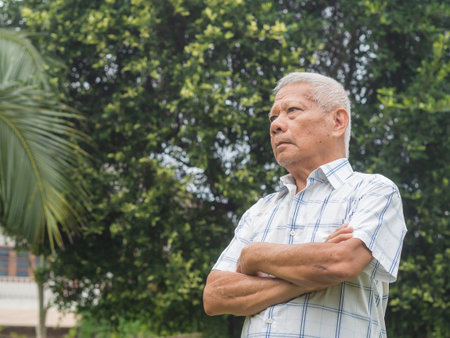 Portrait of a senior man with short gray hair arms crossed looking up while standing in a garden. Aged people and healthcare concept.の写真素材