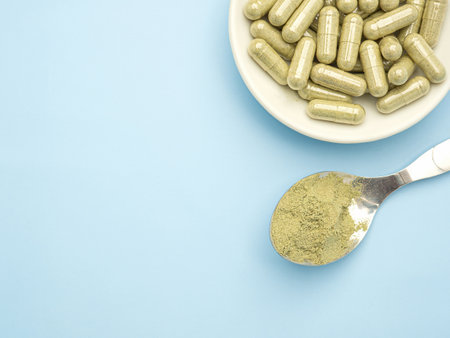 Close-up of Andrographis paniculata powder in spoon and capsules are in a dish isolated on blue background. Herbal, medicine, and healthcare concept.の写真素材