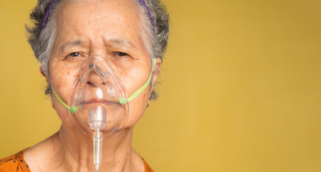 Close-up of a senior woman wearing a medical breathing mask. Sick senior woman wearing an oxygen mask inhalation, pneumonia coronavirus pandemic and undergoing treatment. Space for text.の写真素材