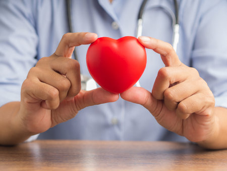 Hand of a doctor showing a red heart shape while sitting in the hospital or clinic. Close-up photo. Space for text. Medical and encouragement concep.の写真素材