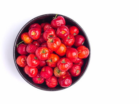 Top view of ripe red acerola cherries fruit in a ceramic bowl isolated on white background. High vitamin C and antioxidant fruits. Close-up photo. Space for text. Concept of healthの写真素材