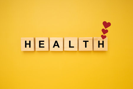 HEALTH word is written on wood blocks with three red heart symbols isolated on a yellow background. Top view. Close-up photo. Health and healthcare concept.の写真素材