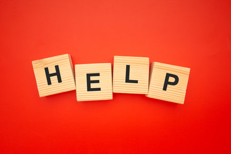 HELP word is written on wood blocks isolated on a red background. Top view. Close-up photo.の写真素材