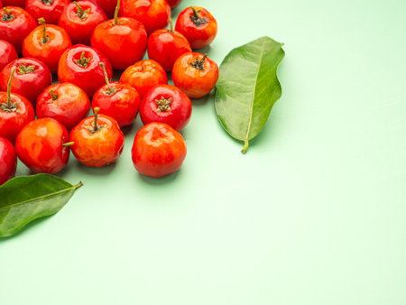 Ripe red acerola cherries fruit and green leaves isolated on a green background. High vitamin C and antioxidant fruits. Top view. Close-up photo. Space for text. Concept of healthy fruits.の写真素材