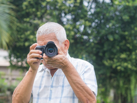 Happy senior man taking photographs with a digital camera while standing outdoors. Aged people photographer and relaxation concept.の写真素材